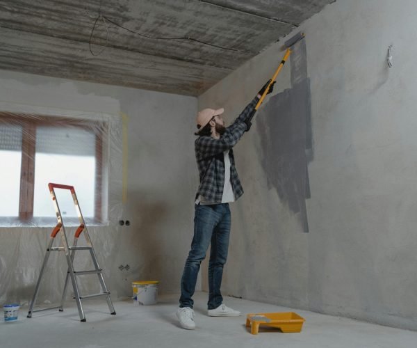 A professional painter is painting a wall in this image, which is used in wall painting section to show the professionalism of wall painting.